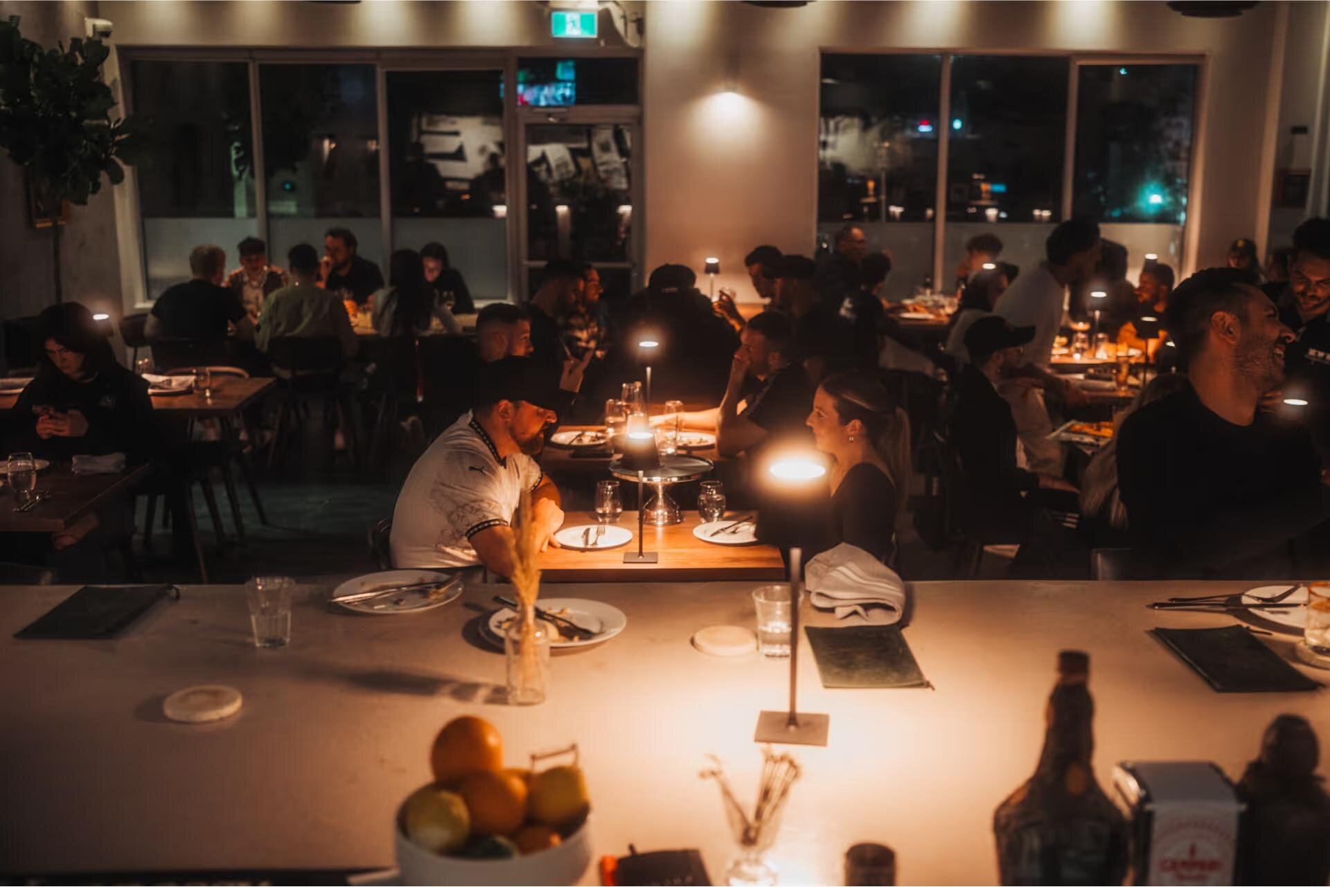 Dinner service at Penelope Social — table lamps, diners, and the bar
