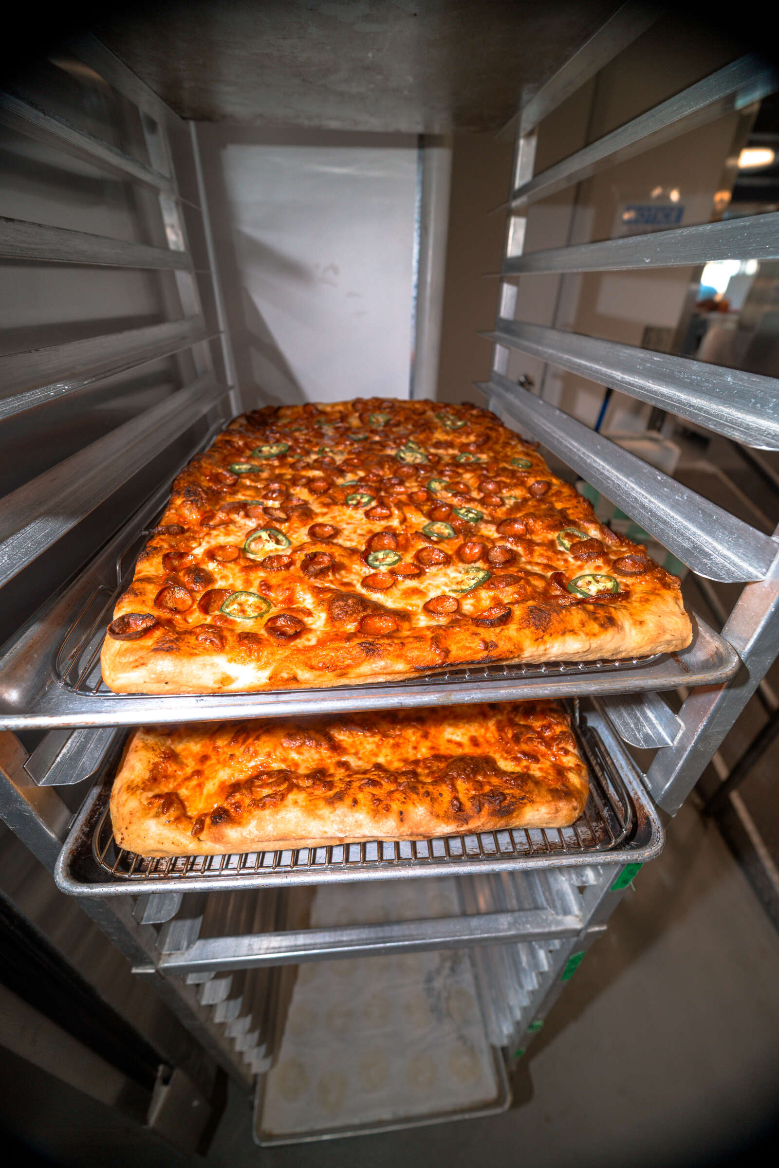 Pans of focaccia and pizza cooling on a rack at Penelope Bakehouse