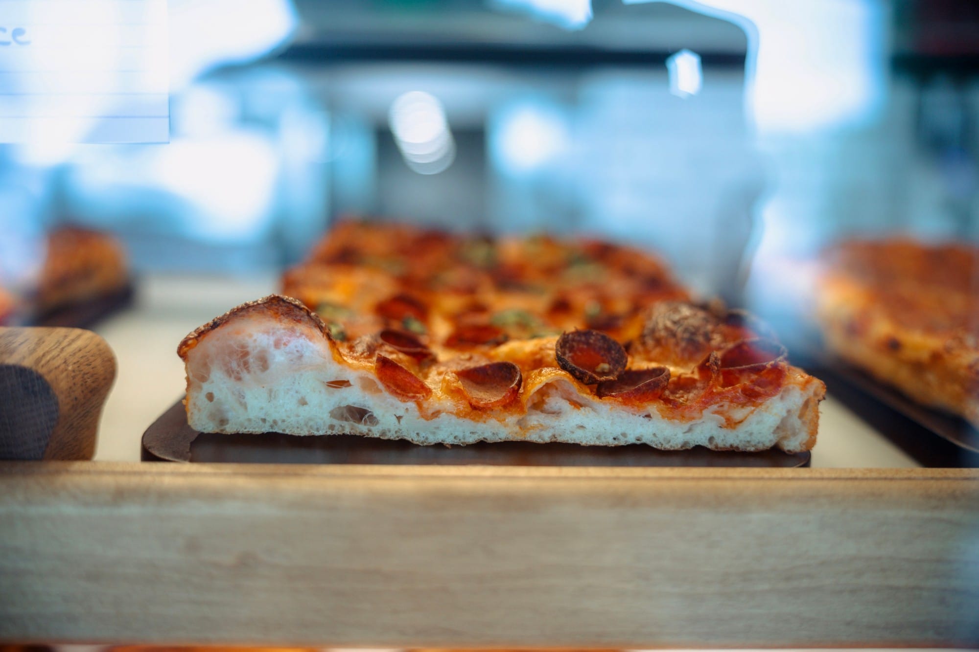 A sourdough pepperoni pizza slice with an airy crumb in the counter case at Penelope Bakehouse in Scarborough